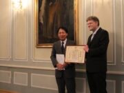 Japonijos ambasadorius Lietuvoje, J.E. Toyoei Shigeeda, įteikia Japonijos užsienio reikalų ministro paskirtą padėkos raštą Azijos studijų centro vadovui Aurelijui Zykui. Kaunas, 2015 m. spalio 23 d.